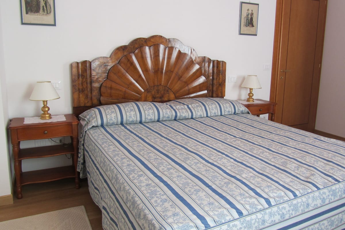 A bedroom with a wooden headboard, a bed with a striped bedspread, two bedside tables with lamps, and a wooden wardrobe.