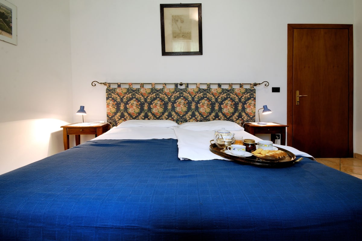 A neatly made bed with a blue bedspread, a tray with breakfast items, and two bedside lamps.