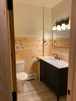 Un baño con paneles de madera, inodoro blanco, lavamanos con espejo y toallero.