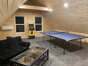 A cozy room with a ping pong table, a black sofa, and a Pac-Man arcade machine.
