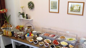 Una mesa de buffet con diversos alimentos y condimentos, una planta en maceta y una estantería con objetos decorativos.