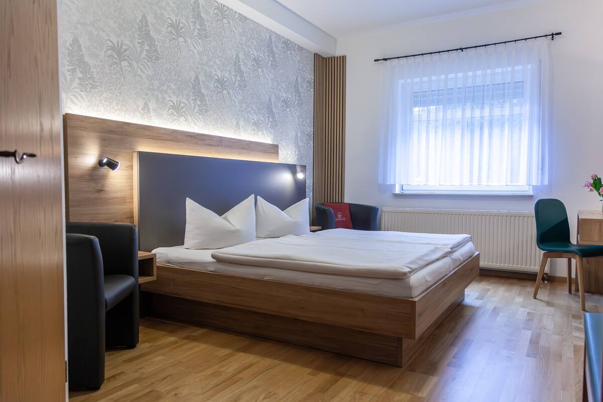 Un dormitorio moderno con una cama de madera, una mesita de noche, una silla y una ventana con cortinas.