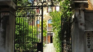 A wrought iron gate with a keyhole, leading to a paved pathway. - Testa - WR Apartments (Venice)