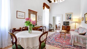 A dining area with a round table, chairs, and a vase of flowers. There is a sofa and a television in the living area. - Testa - WR Apartments (Venice)