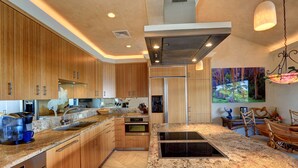 Una cucina moderna con mobili in legno, piani in granito, forno integrato e una grande isola con piano cottura.