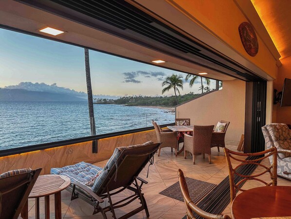 A balcony with wicker furniture, a table, and a view of the ocean.