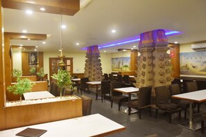 A restaurant with wooden tables and chairs, decorative pillars, and a mural on the wall.