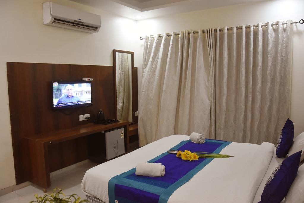 A hotel room with a bed, a TV on a wooden stand, a desk with a chair, and a window with curtains.