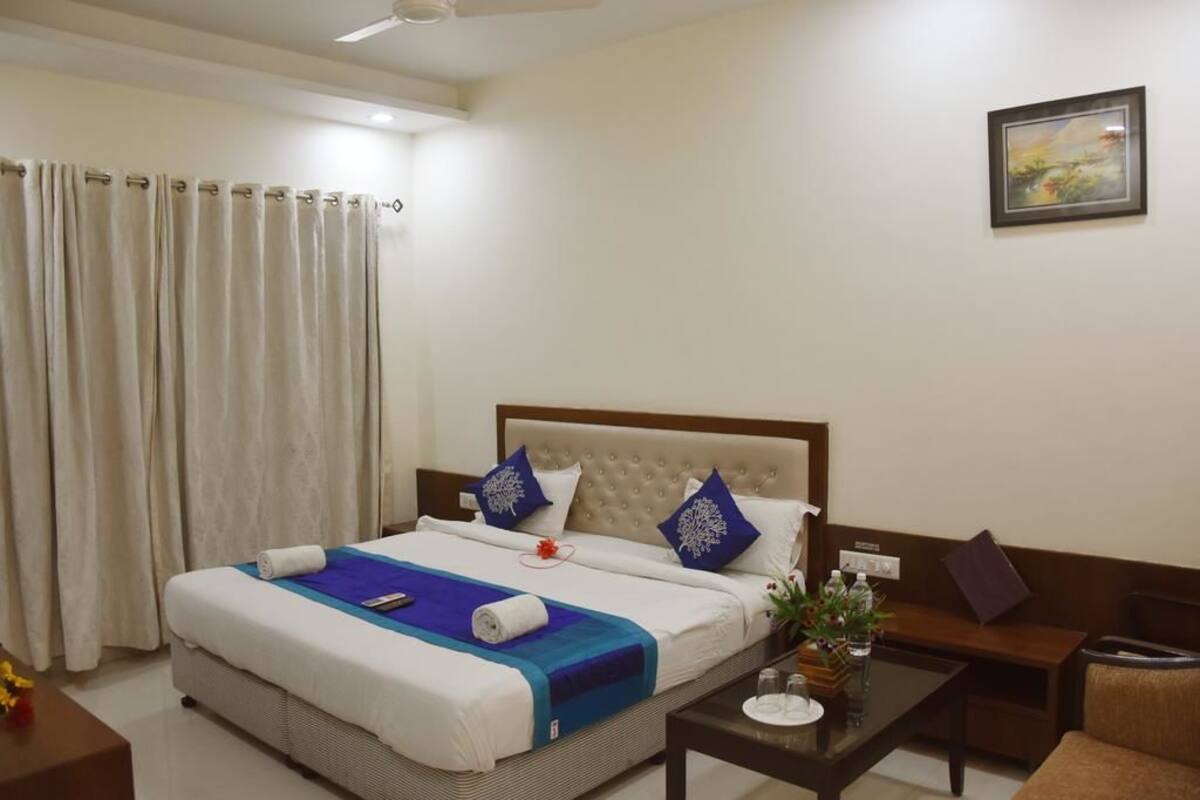 Una habitación de hotel ordenada con una cama, una mesita, una silla, un sofá y un cuadro en la pared.