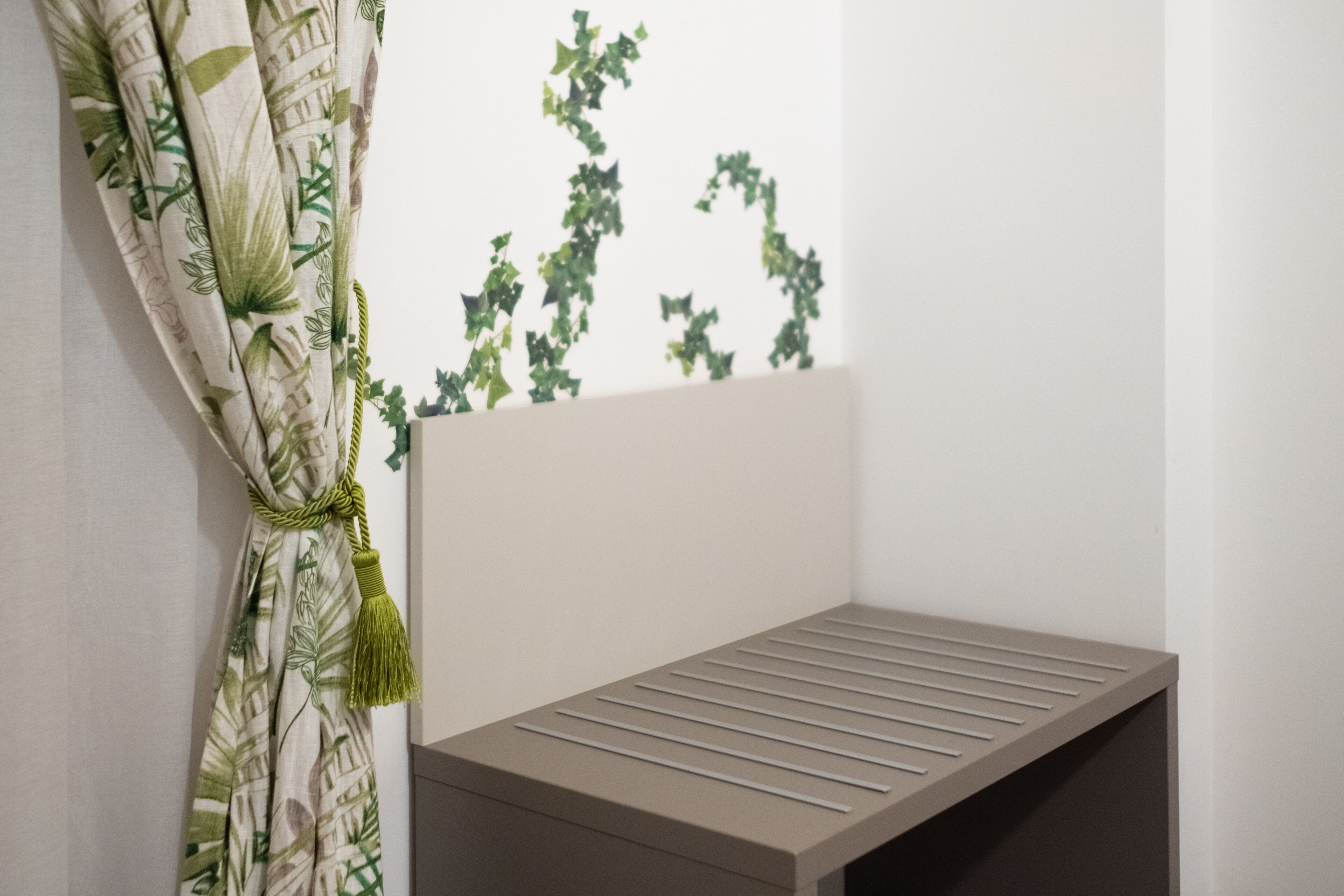A room with a bed, a window with a curtain, and a plant on the windowsill.