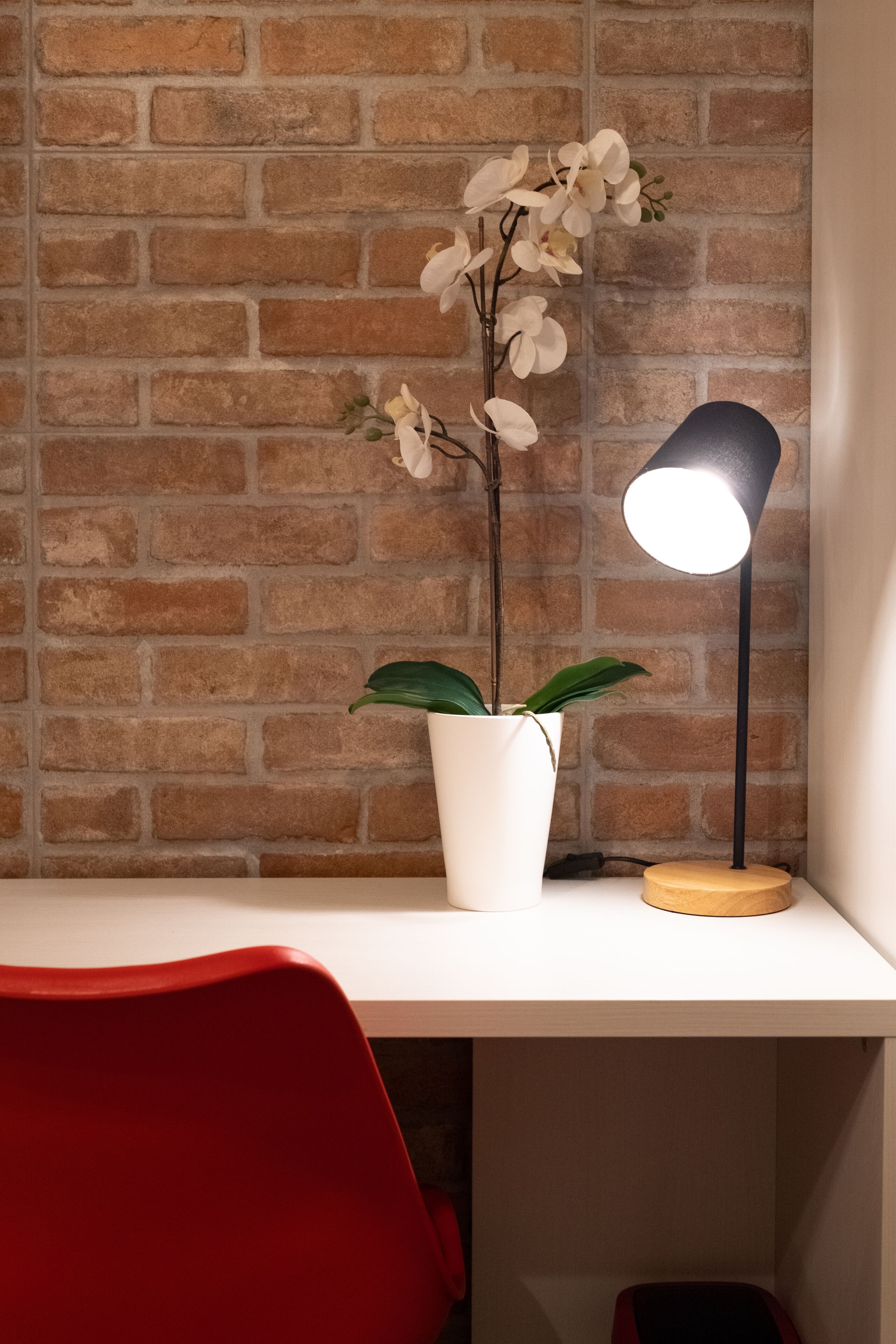 A desk with a white vase containing a plant and a black desk lamp.