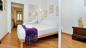 Une chambre à coucher avec un lit, un plancher en bois, un bureau avec une lampe et un miroir au mur.