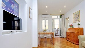 Un salon moderne avec un plancher en bois, un téléviseur fixé au mur, une table à manger avec des chaises et une commode en bois.