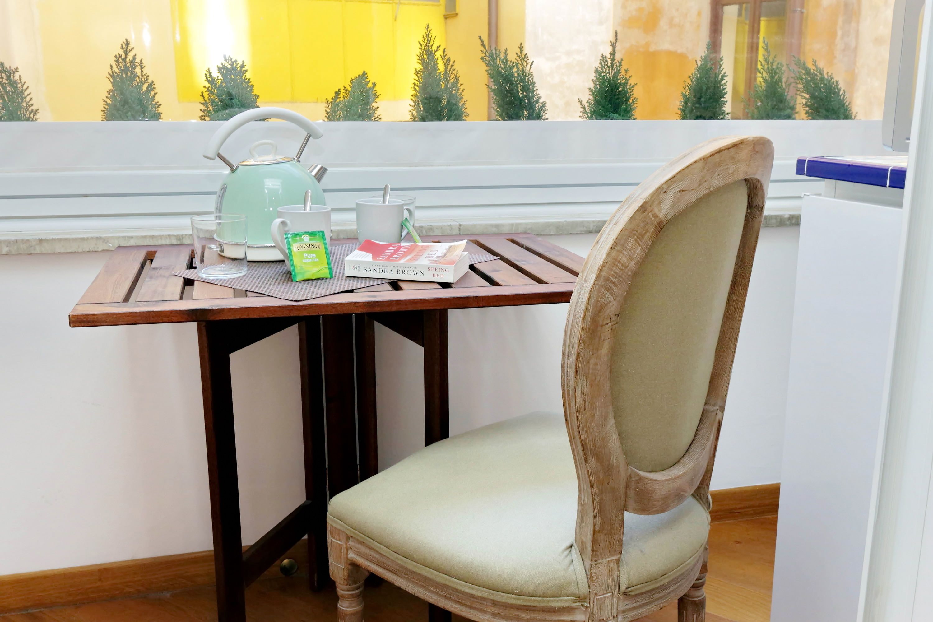 A wooden table with a chair, a kettle, a mug, and a book.