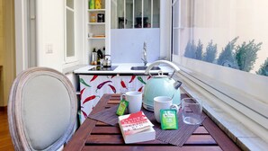 Une petite cuisine avec une fenêtre, une table sur laquelle se trouvent un livre, des sachets de thé et une bouilloire.
