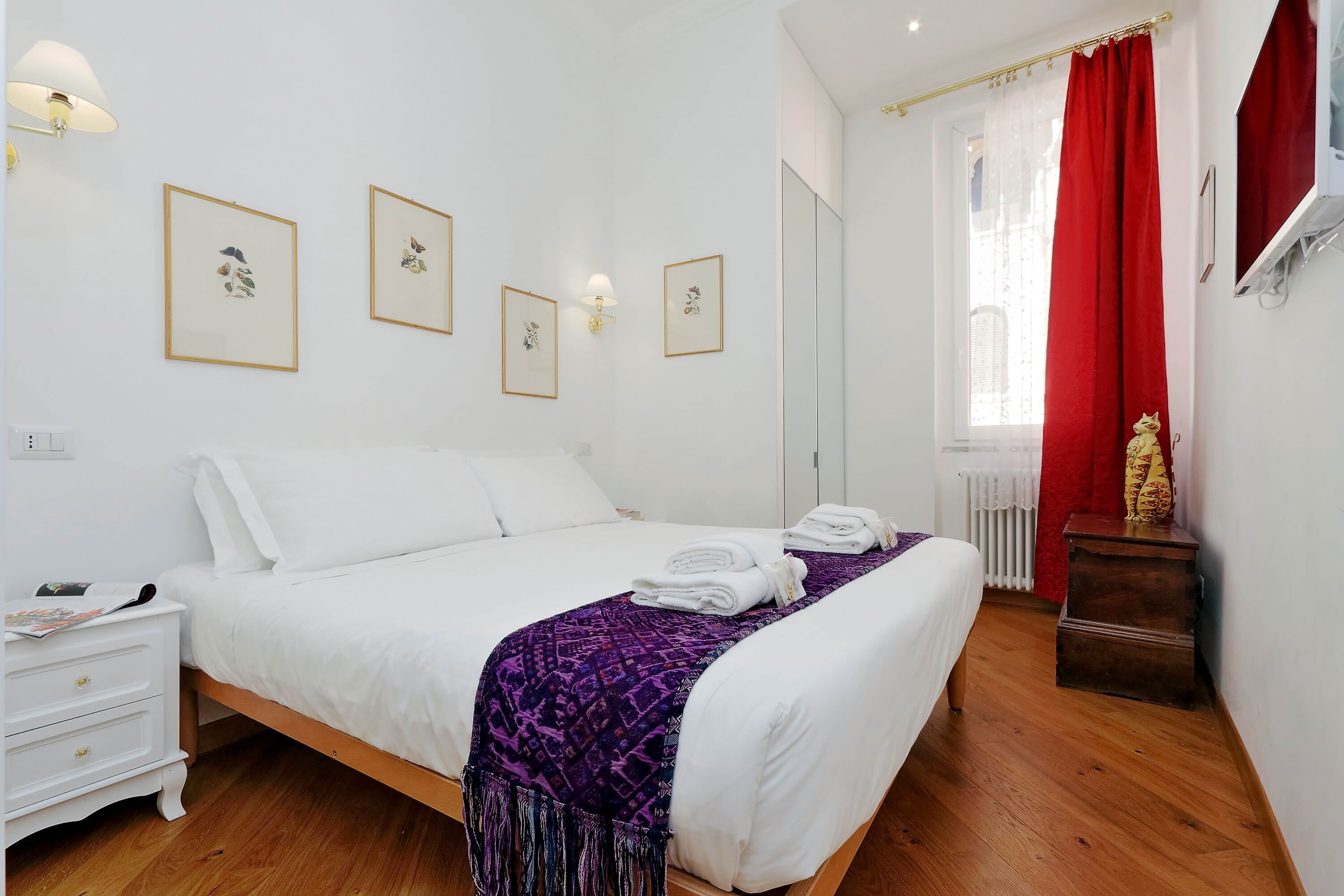 A neatly arranged bedroom with a bed, white nightstand, and a small wooden stool.