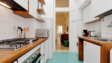 Una cocina compacta con gabinetes blancos, una encimera de madera, una estufa a gas y un microondas.