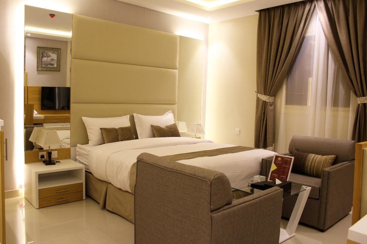 A hotel room with a large bed, a sofa, a TV, and a nightstand.