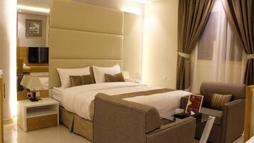 A hotel room with a large bed, a sofa, a TV, and a nightstand.