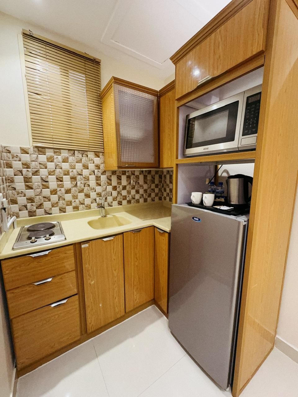 A compact kitchen with wooden cabinets, a stainless steel refrigerator, a microwave, and a sink.