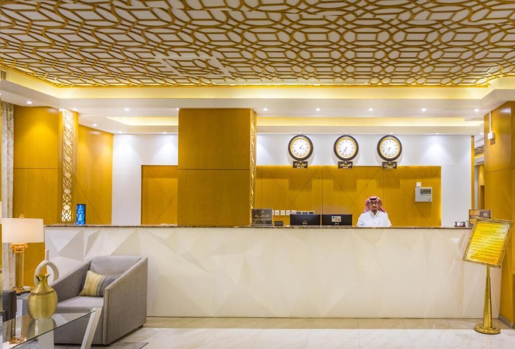 A hotel reception area with a receptionist, a reception desk, and three clocks on the wall.
