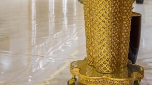 Una mesa dorada y ornamentada con diseños intrincados, superficie reflectante y un pequeño pedestal.