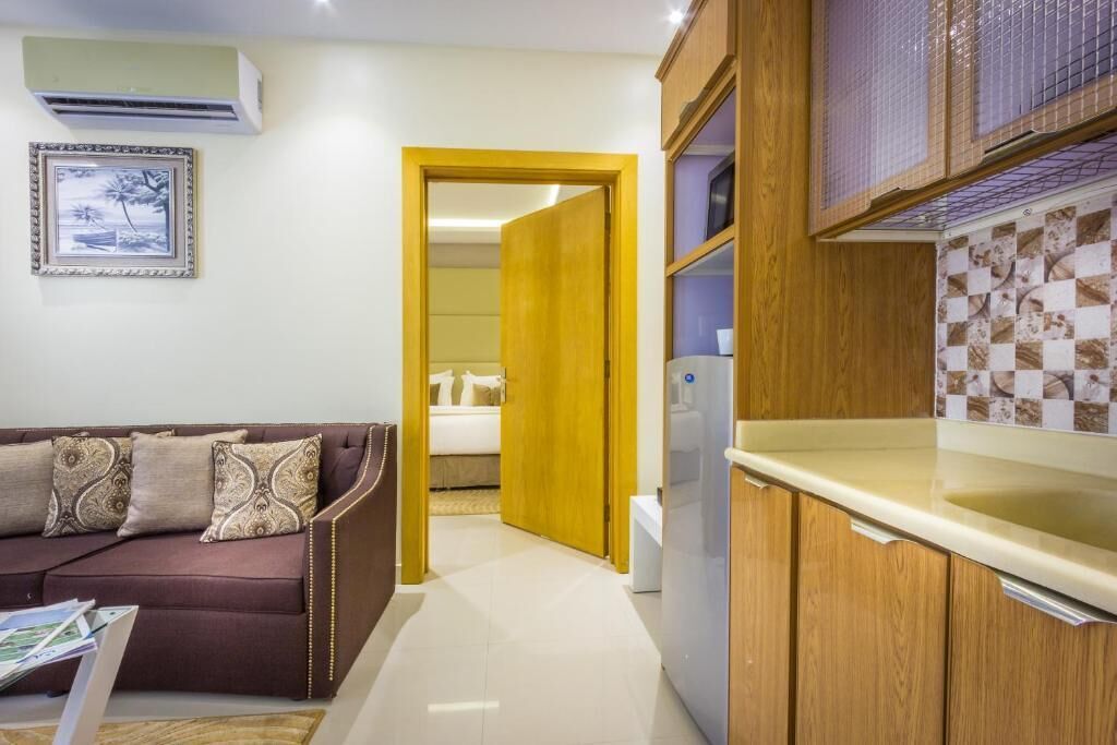Un espacio habitable compacto con sofá, zona de cocina y una puerta que da a un dormitorio.