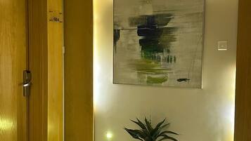 A hallway with a wooden door, a potted plant, and a large abstract painting on the wall.