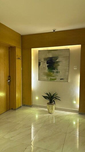 A hallway with a wooden door, a potted plant, and a large abstract painting on the wall. - AL Muhaidb Residence Abha - Economic (Abha)