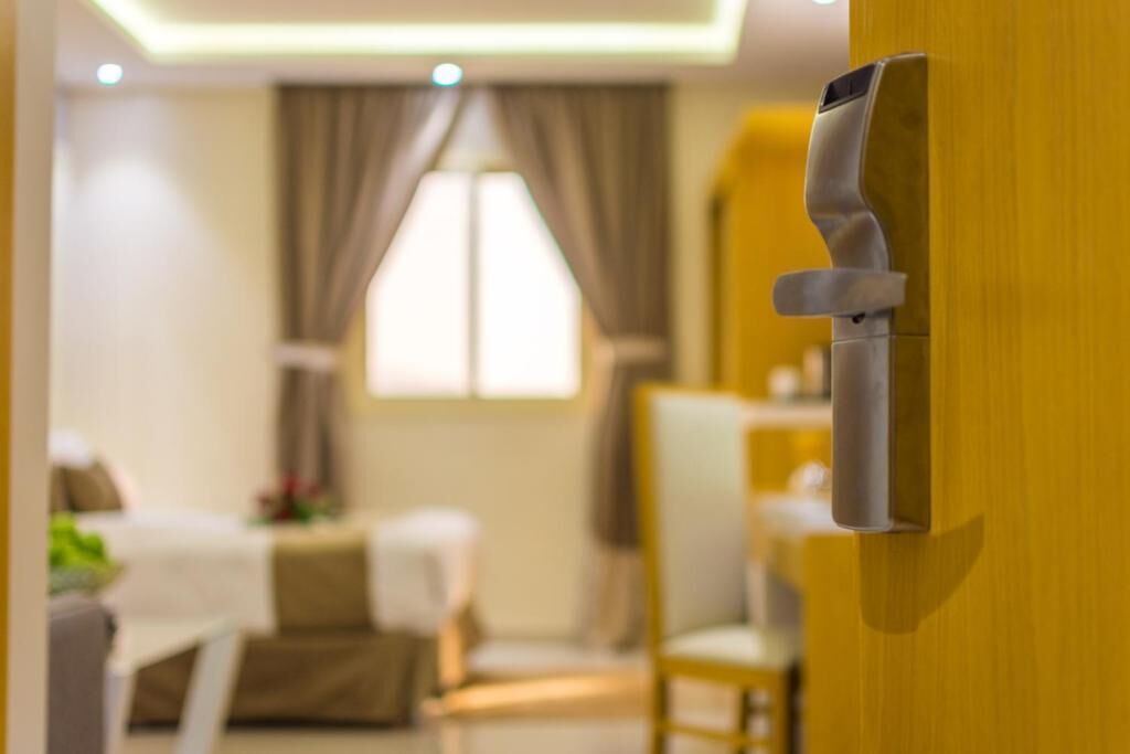 A hotel room with a wooden door, a dining area with a table and chairs, and a window with curtains.