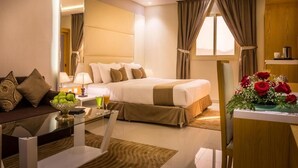Habitación de hotel con una cama, un sofá, una mesa con frutero, una lámpara y un jarrón de flores.