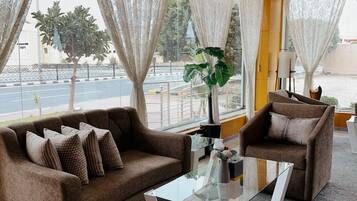 A modern hotel room with a sofa set, a glass coffee table, and a view of the street through large windows.
