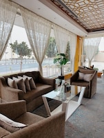 A modern hotel room with a sofa set, a glass coffee table, and a view of the street through large windows.
