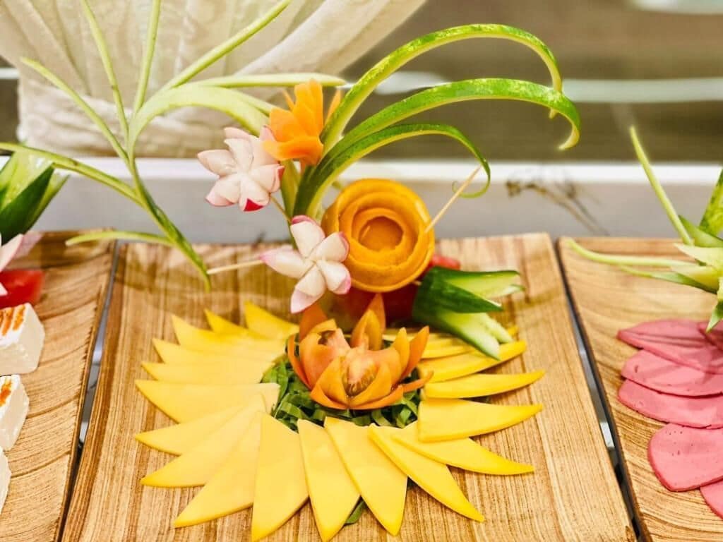 A wooden table with a decorative arrangement featuring a yellow flower and green leaves.