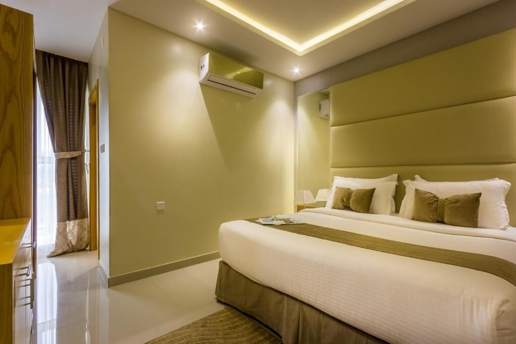 A modern hotel room with a large bed, a bedside table, a lamp, and an air conditioning unit.