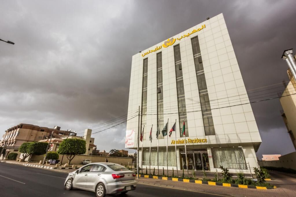 A modern building with a sign reading 'Al Wasl Al-Rashid Residence' and multiple flags.