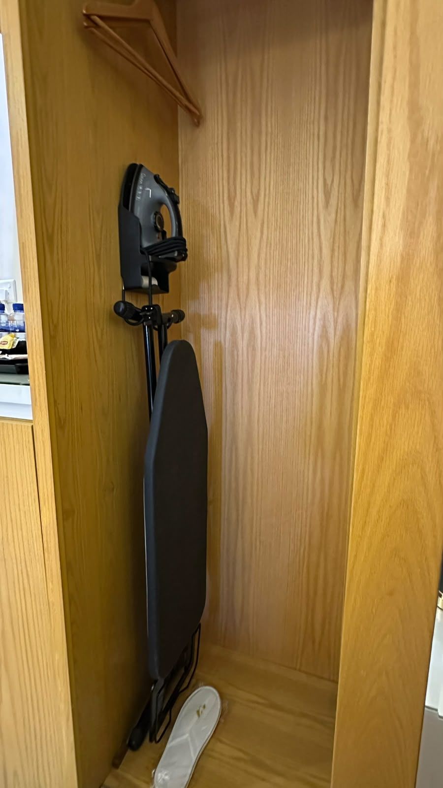 A wooden cabinet with a black object on a stand, a white object on the floor, and a wooden door.