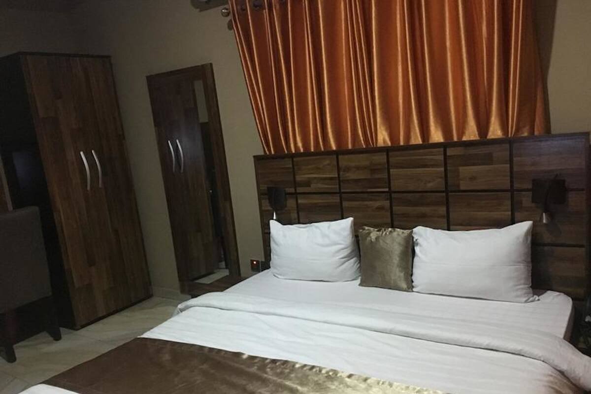 A bedroom with a wooden headboard, a bed with white and beige bedding, and a brown accent piece.