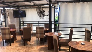 Un café con mesas y sillas redondas, una pantalla de televisión y ventiladores.