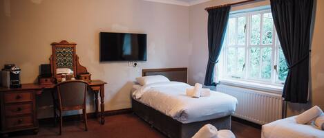 A hotel room with a bed, a desk with a chair, a television, and a window with curtains.