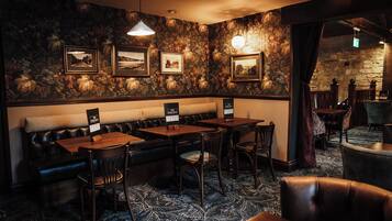 A restaurant with a stone wall, framed pictures, a wooden bench, and tables with chairs.