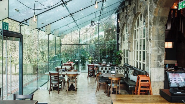 Un restaurant doté d’une véranda en verre, de meubles en bois et de murs en pierre.