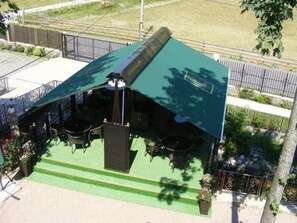 Un pequeño edificio con techo verde, mesas al aire libre y un patio.