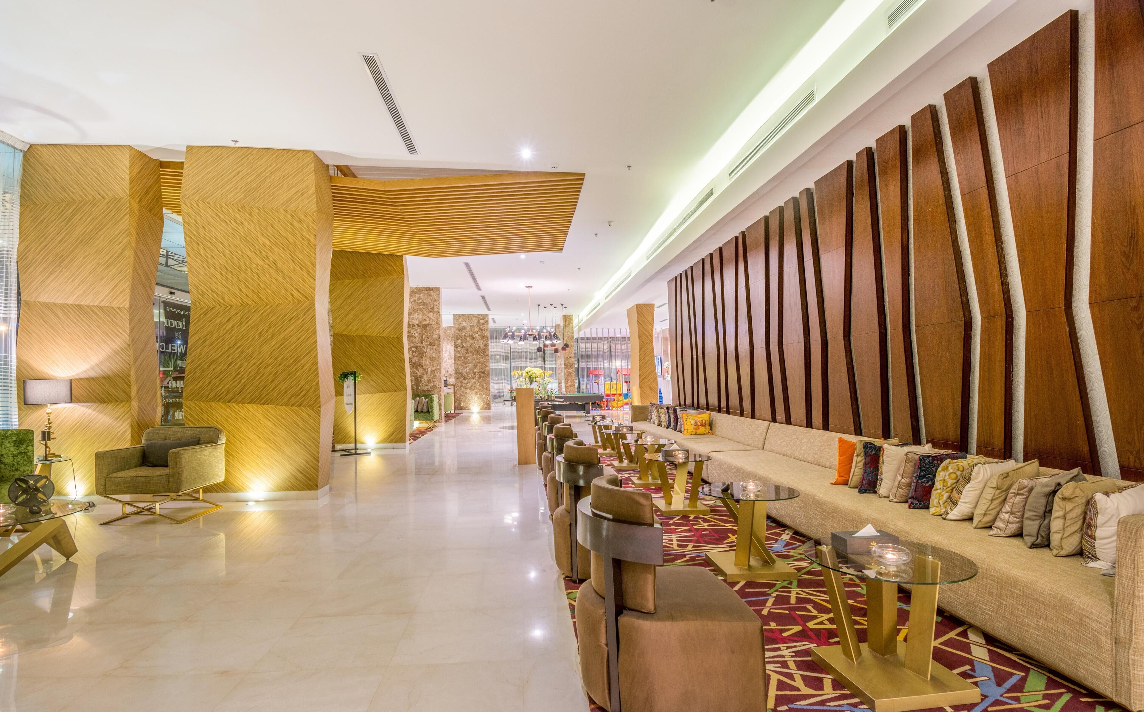 Eine großzügige Lobby mit modernem Design, ausgestattet mit einer langen Couch, mehreren Sitzbereichen und einer Wand mit vertikalen Holzlatten.
