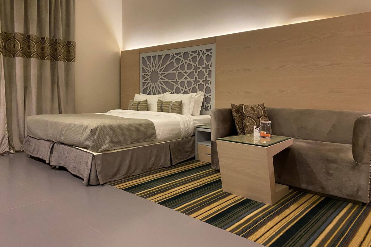 A hotel room with a bed, a sofa, a nightstand, and a decorative wall panel.