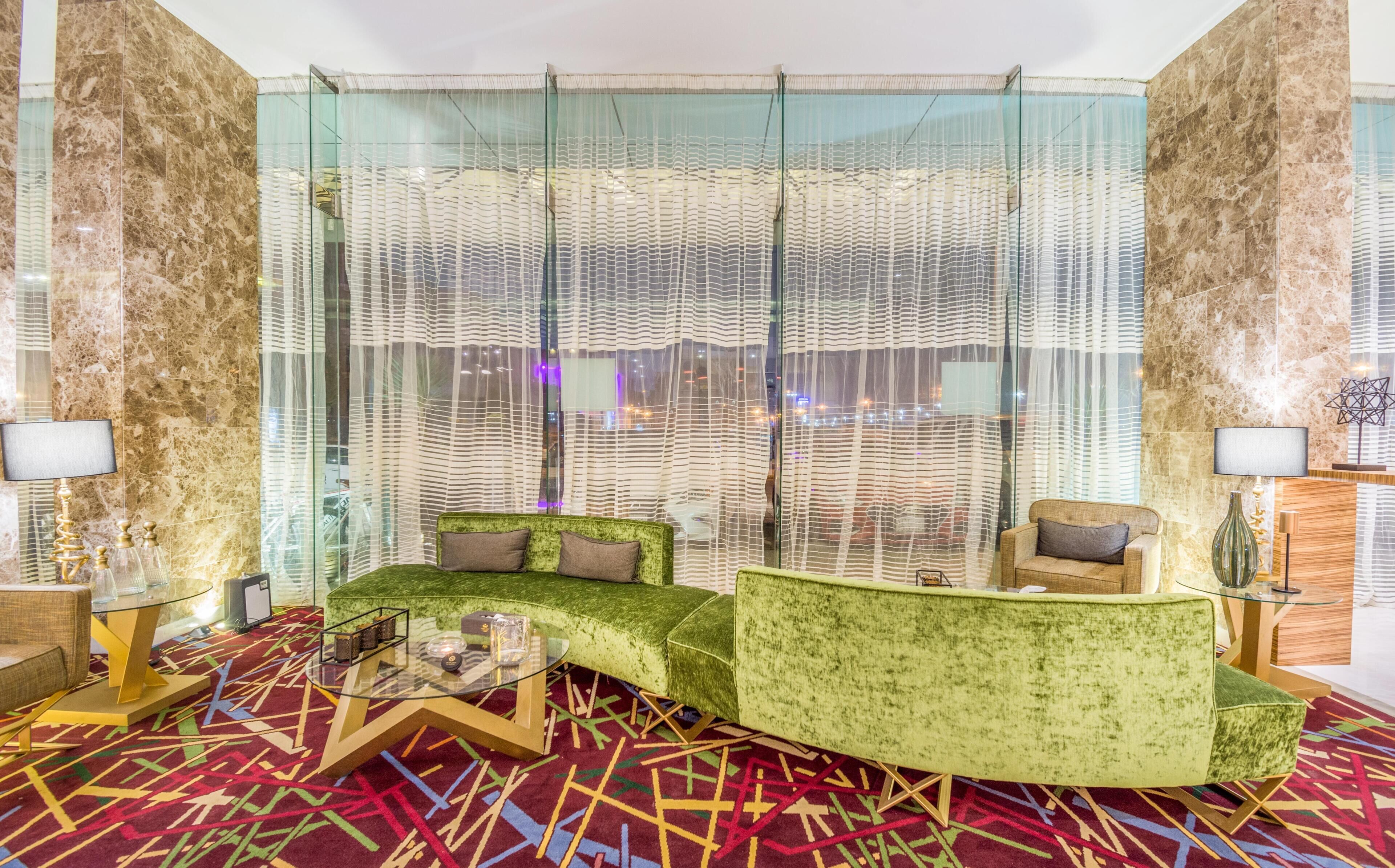 A modern living room with green sofas, a glass coffee table, and a patterned carpet.