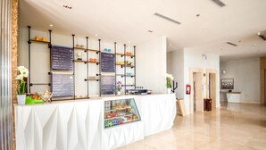 A clean, modern reception area with a white reception desk, a glass display case, and a menu board listing various drinks and services. - Ewaa Express Hotel - Al hamra (Jeddah)