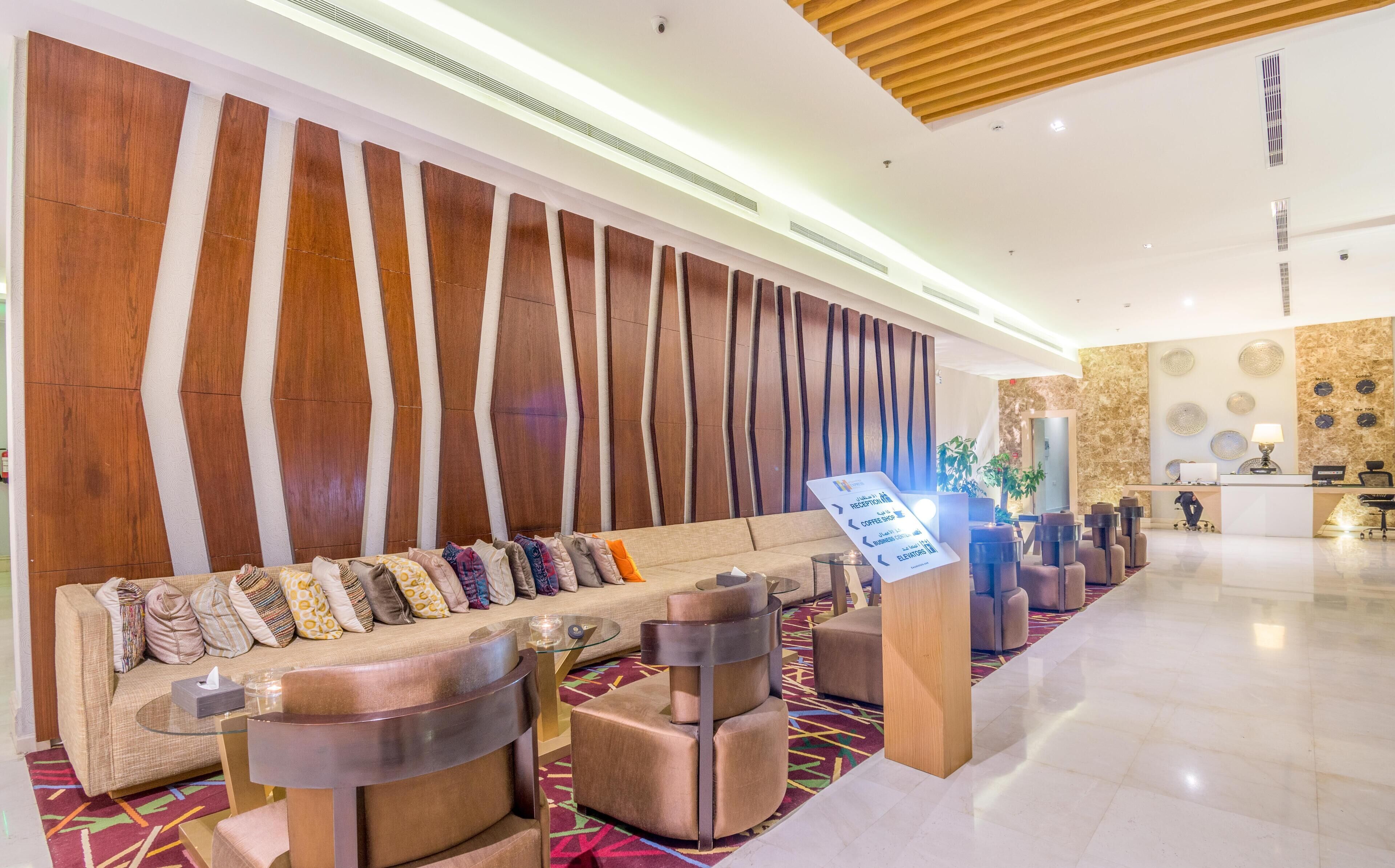 Um lobby moderno com um balcão de recepção extenso, um sofá com almofadas estampadas e uma parede decorativa com painéis de madeira.