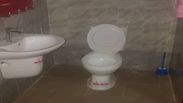 Un baño con inodoro y lavamanos blancos, y un trapeador azul.