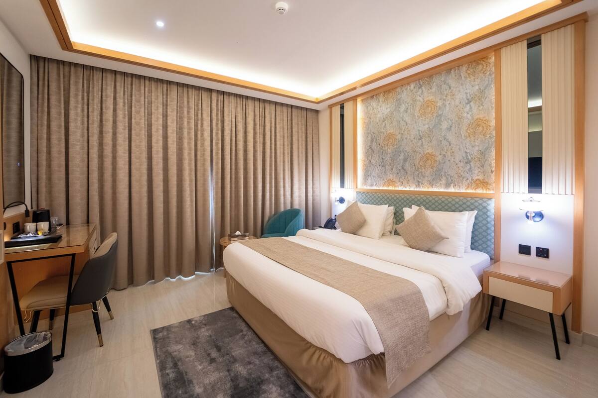 A modern hotel room with a large bed, a desk, and a chair.